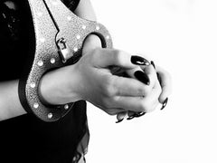 Close-up of hands with black nails locked in the Heavy Aluminum Cangue with Padlock Bondage Yoke Shrews Fiddle Restraint by The Cuffstore, worn over dark clothing against a white background.