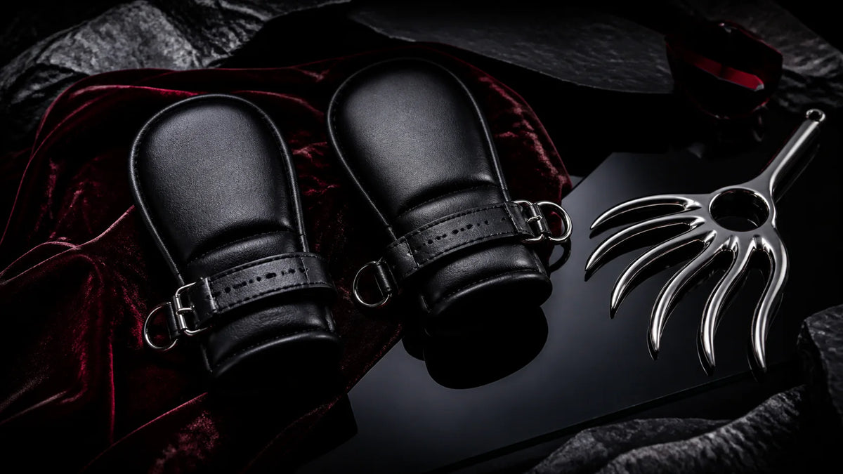 Padded black leather fist mitts with silver hardware beside a stainless claw.