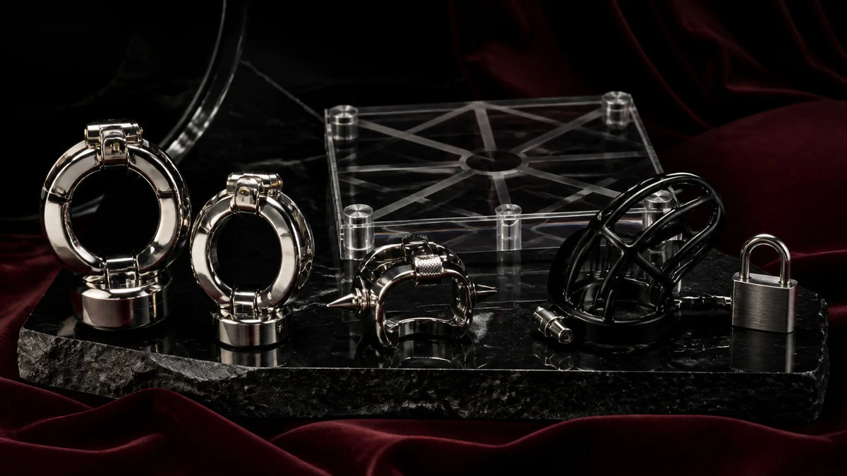 Polished weighted rings, clear acrylic hardware, and a black metal cage form on stone.