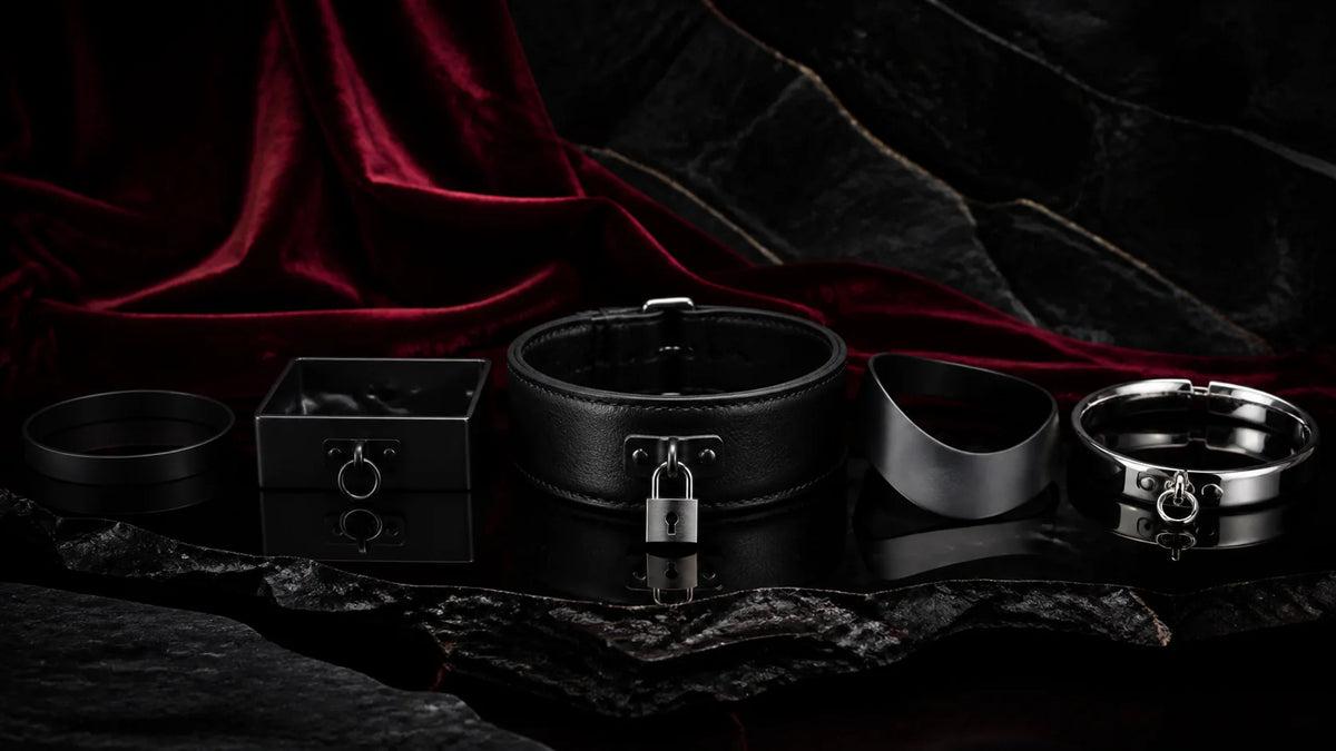 Black leather and matte-metal collars with a small padlock on dark stone.