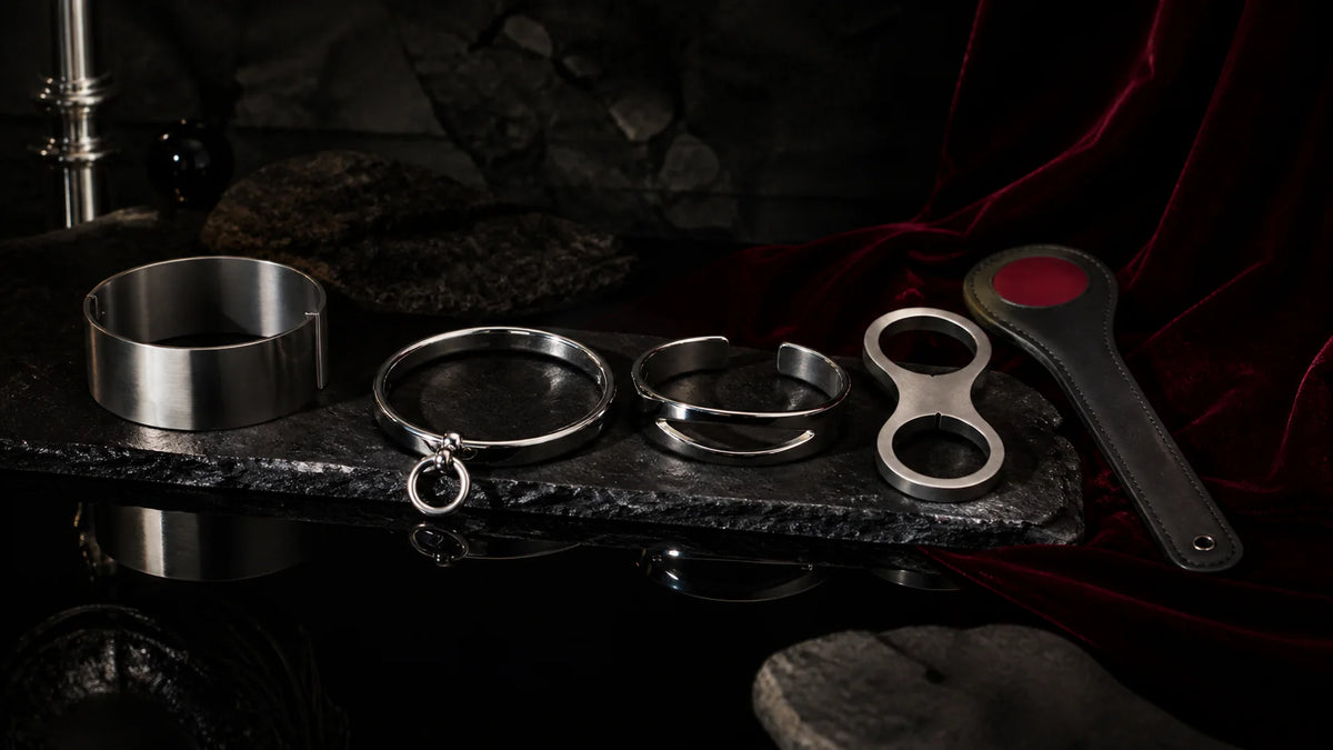 Mixed-finish stainless collars and cuffs with a red-inlay leather paddle on dark stone.