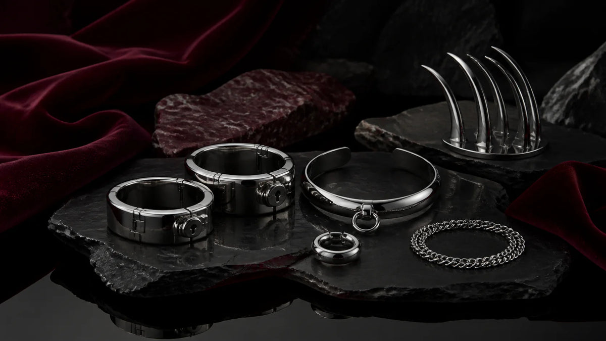 Polished stainless cuffs, a curved collar, and a small ring arranged on dark stone.