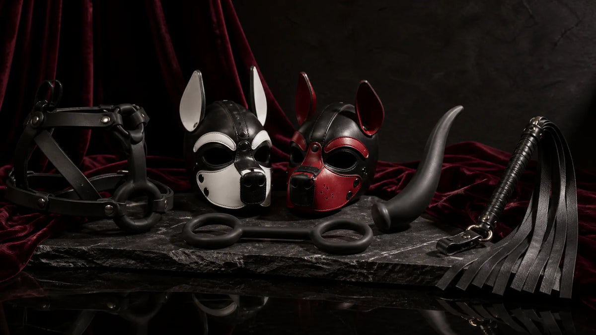 Leather play masks, silicone tail-shaped forms, and a compact flogger on dark velvet.