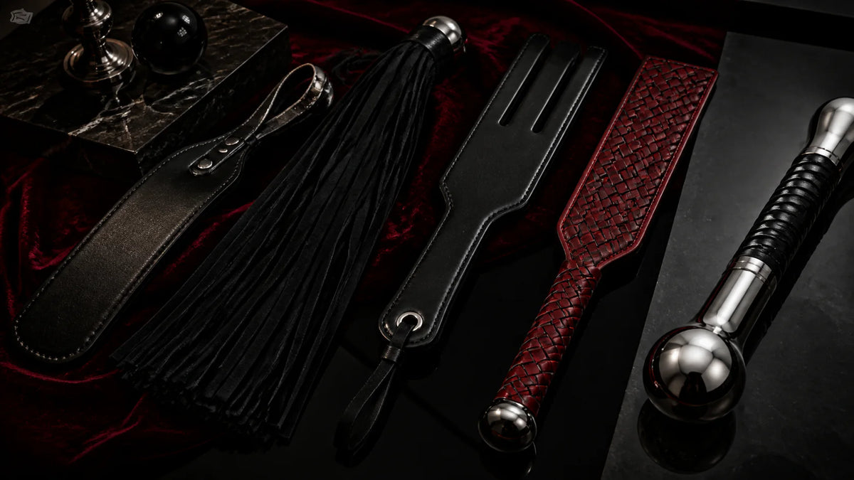 Leather paddles and a multi-tail flogger arranged on oxblood velvet.
