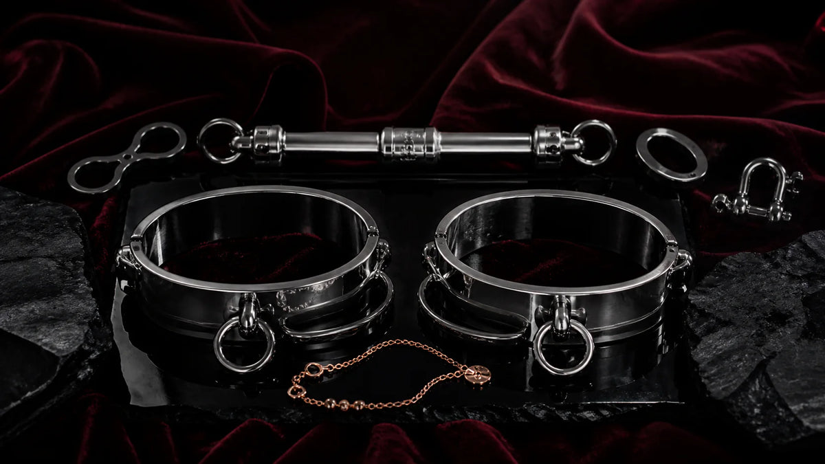 Polished elliptical ankle cuffs and a compact spreader bar on dark stone.