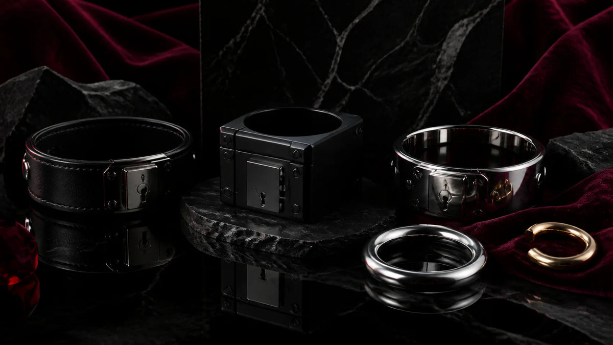 A rigid black choker, matte-black collar, and polished eternity collar on obsidian.