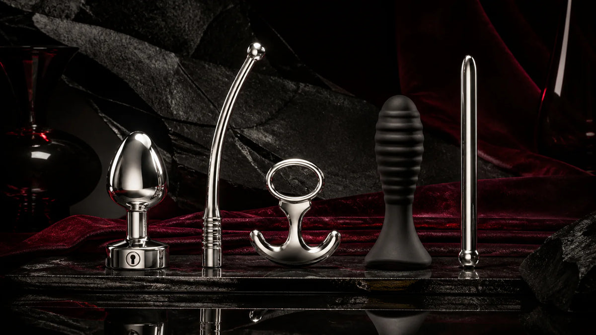 Rounded stainless and dark silicone plug forms with a curved wand on obsidian.