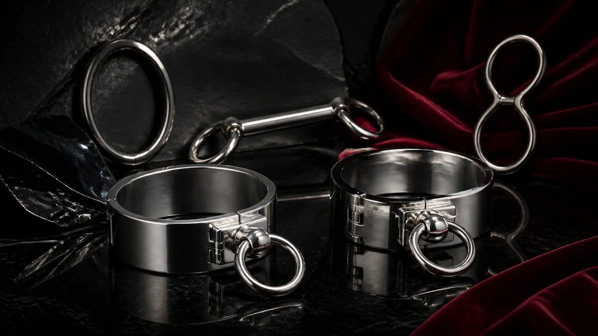 Polished stainless wrist cuffs linked by a short chain on black stone.