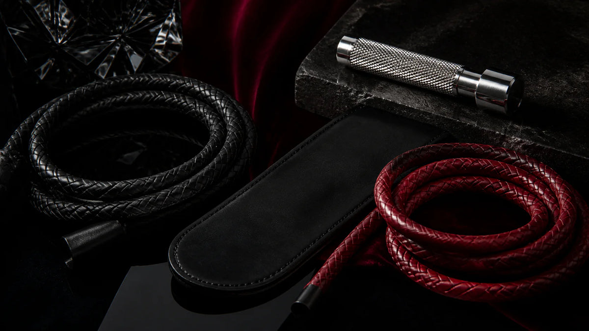 Black and red leather paddles and suede floggers arranged on oxblood velvet.
